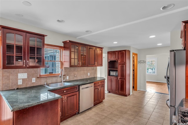 kitchen with appliances with stainless steel finishes, dark stone countertops, a wealth of natural light, and sink