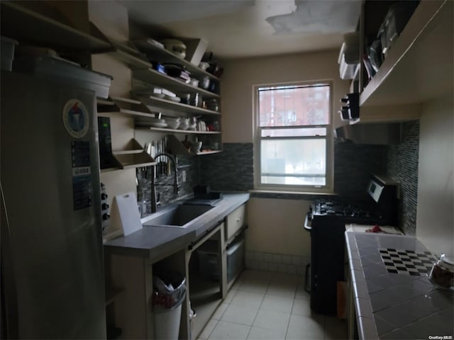 kitchen featuring stove, refrigerator, sink, light tile patterned floors, and tile counters