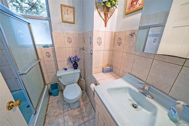 full bathroom featuring tile patterned floors, combined bath / shower with glass door, toilet, vanity, and tile walls