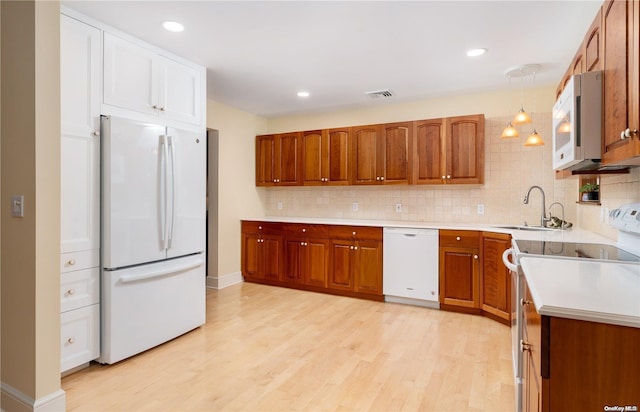 kitchen featuring light wood-type flooring, tasteful backsplash, white appliances, sink, and decorative light fixtures