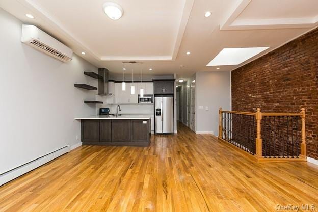 kitchen featuring light hardwood / wood-style flooring, wall chimney exhaust hood, baseboard heating, appliances with stainless steel finishes, and a wall unit AC