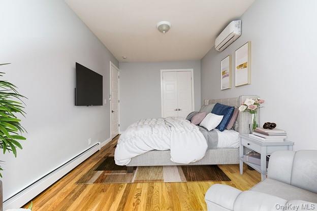 bedroom with a wall mounted AC, wood-type flooring, and baseboard heating