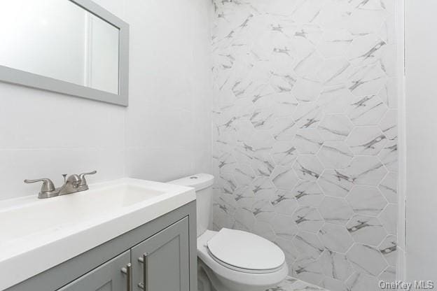 bathroom featuring tiled shower, vanity, and toilet