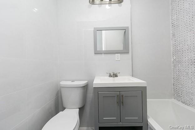 bathroom featuring vanity, tile walls, and toilet