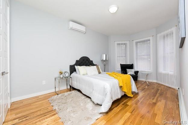 bedroom with a baseboard radiator, a wall mounted air conditioner, and hardwood / wood-style flooring