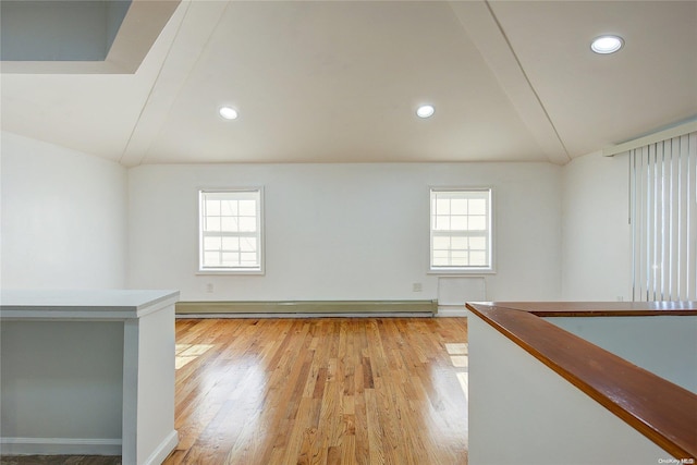 spare room with a baseboard radiator, a healthy amount of sunlight, vaulted ceiling, and light hardwood / wood-style floors