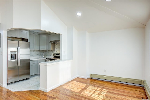 kitchen featuring a baseboard heating unit, vaulted ceiling, decorative backsplash, appliances with stainless steel finishes, and light hardwood / wood-style floors