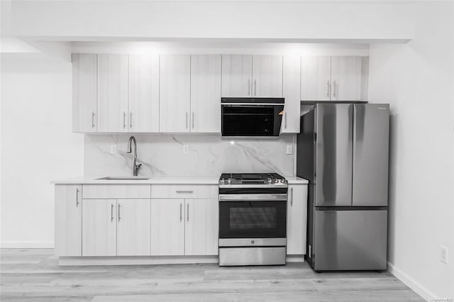 kitchen featuring sink, light wood-type flooring, appliances with stainless steel finishes, tasteful backsplash, and white cabinetry