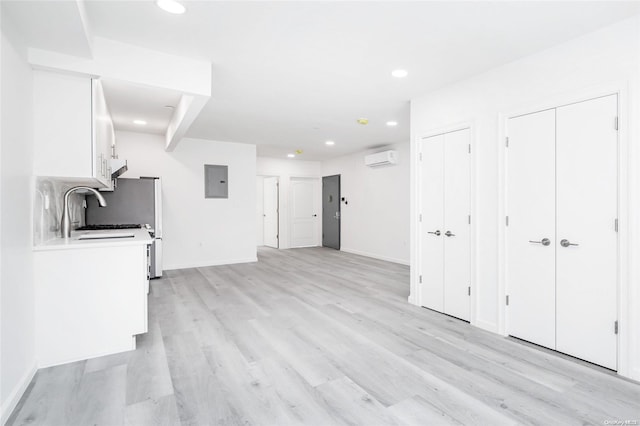 unfurnished living room with a wall unit AC, electric panel, light hardwood / wood-style flooring, and sink