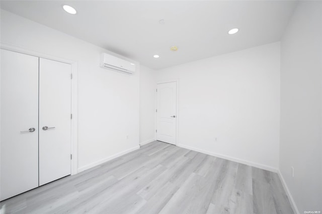 unfurnished bedroom featuring a closet, a wall mounted air conditioner, and light wood-type flooring