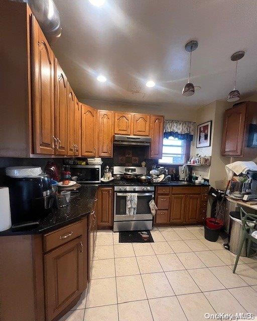 kitchen featuring under cabinet range hood, stainless steel appliances, hanging light fixtures, brown cabinetry, and dark countertops