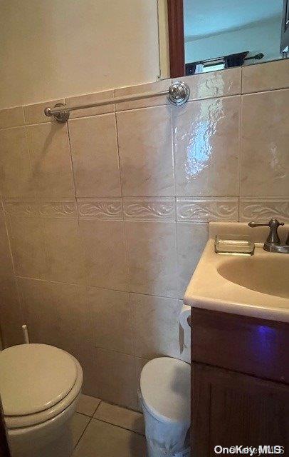 bathroom with toilet, vanity, tile walls, and tile patterned floors