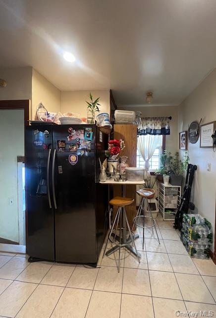 kitchen featuring light tile patterned floors, a peninsula, a kitchen bar, and freestanding refrigerator