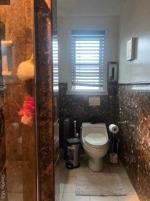 full bathroom with toilet, a stall shower, tile walls, and tile patterned floors