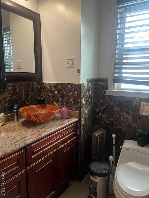 half bath with toilet, radiator heating unit, tile walls, and vanity