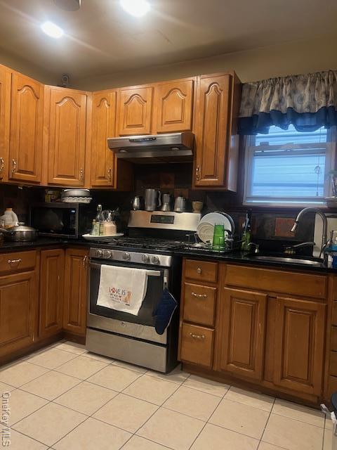 kitchen with dark countertops, stainless steel range with gas stovetop, a sink, black microwave, and under cabinet range hood