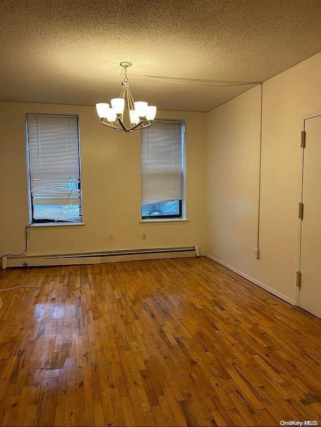 spare room featuring baseboard heating, a chandelier, a textured ceiling, and wood-type flooring