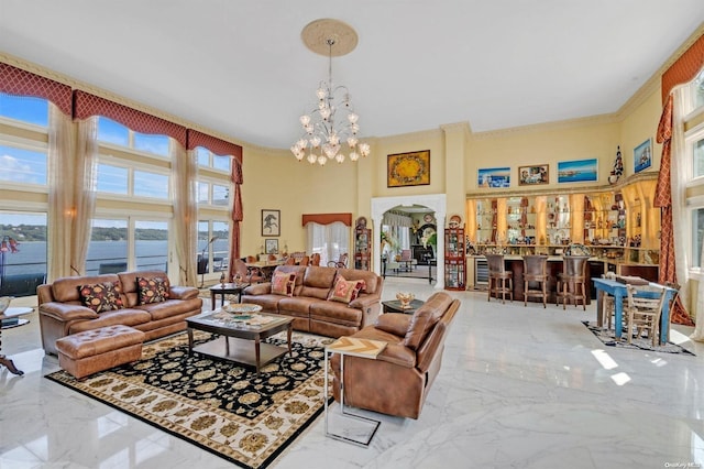 living room featuring a high ceiling, a notable chandelier, bar area, a water view, and ornamental molding