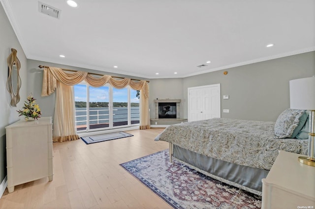 bedroom with a closet, light hardwood / wood-style flooring, a water view, and ornamental molding