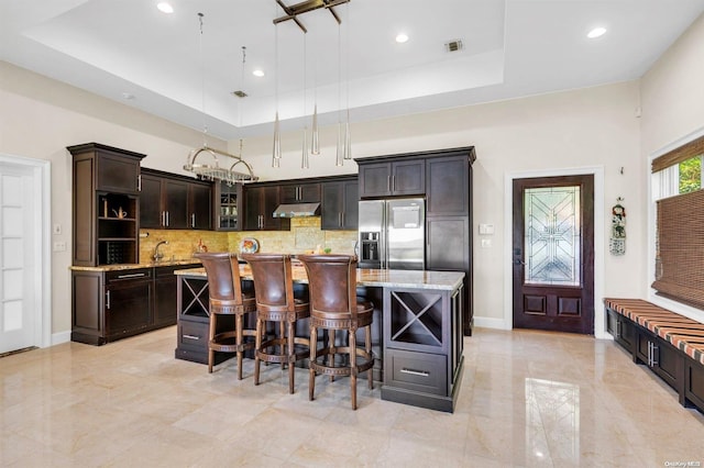 kitchen with a kitchen island, stainless steel refrigerator with ice dispenser, and a tray ceiling