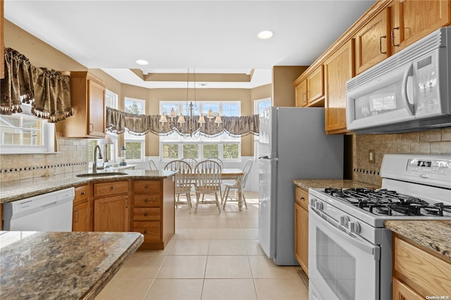 kitchen featuring light stone countertops, tasteful backsplash, white appliances, sink, and an inviting chandelier