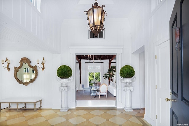 foyer with a high ceiling, wooden walls, light hardwood / wood-style floors, and a notable chandelier