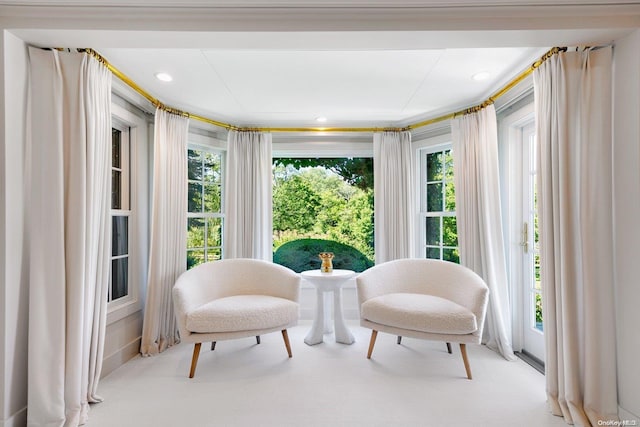 living area featuring light carpet, crown molding, and a healthy amount of sunlight