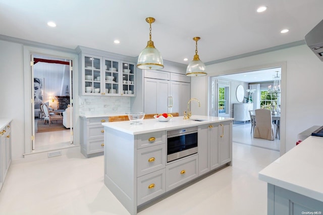 kitchen featuring backsplash, crown molding, sink, pendant lighting, and an island with sink