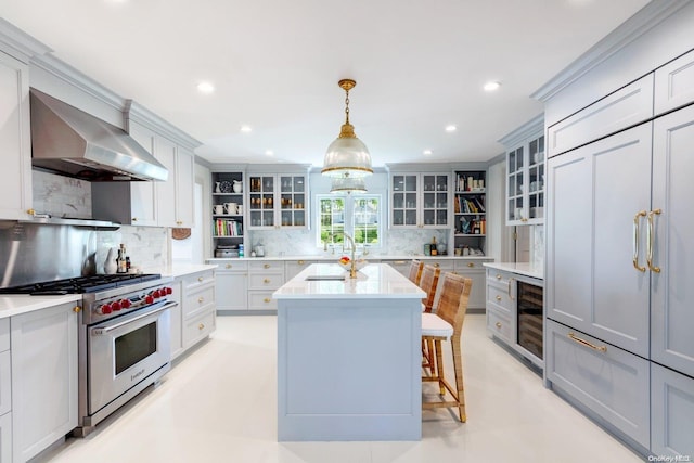 kitchen featuring wall chimney exhaust hood, hanging light fixtures, beverage cooler, premium stove, and a center island with sink