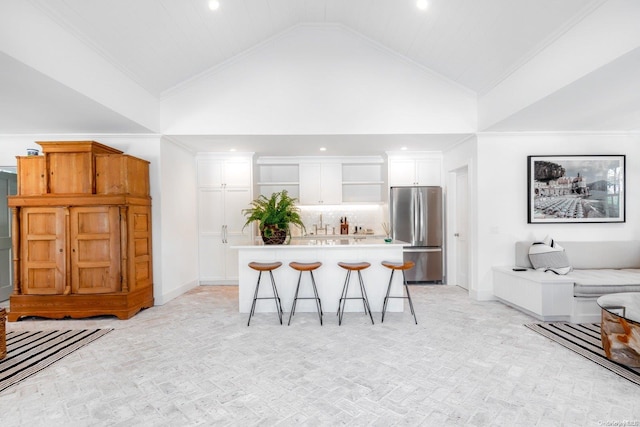 kitchen with high vaulted ceiling, a kitchen bar, white cabinetry, and stainless steel refrigerator