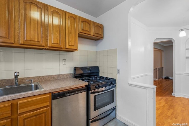 kitchen with tasteful backsplash, sink, stainless steel appliances, and light wood-type flooring