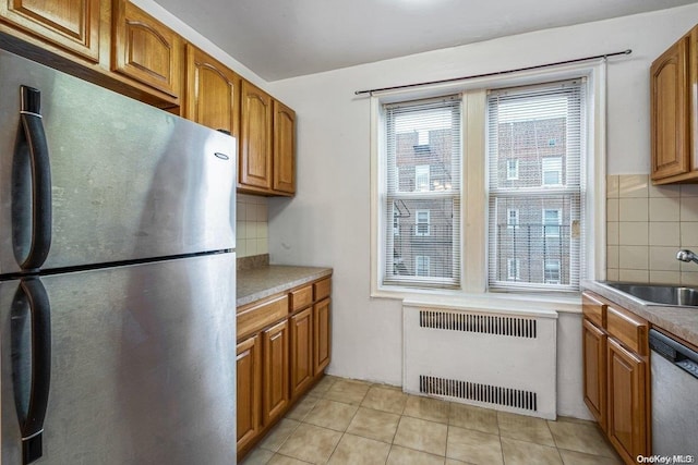 kitchen featuring backsplash, sink, light tile patterned flooring, radiator heating unit, and stainless steel appliances