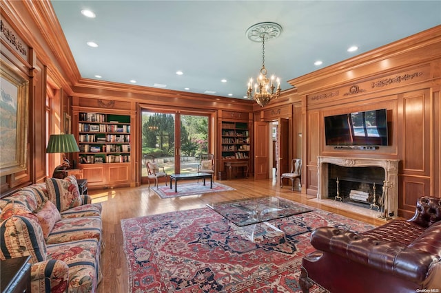 living room featuring crown molding, light hardwood / wood-style flooring, built in shelves, a premium fireplace, and a notable chandelier