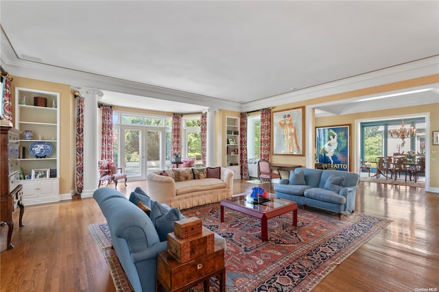 living room featuring an inviting chandelier, light hardwood / wood-style flooring, built in features, ornate columns, and ornamental molding