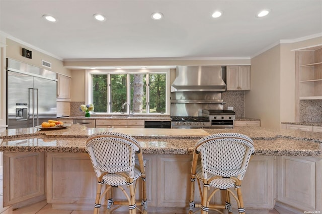 kitchen featuring light stone countertops, wall chimney range hood, appliances with stainless steel finishes, and tasteful backsplash