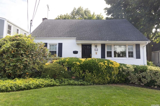 view of front facade with a shingled roof, a front lawn, and brick siding