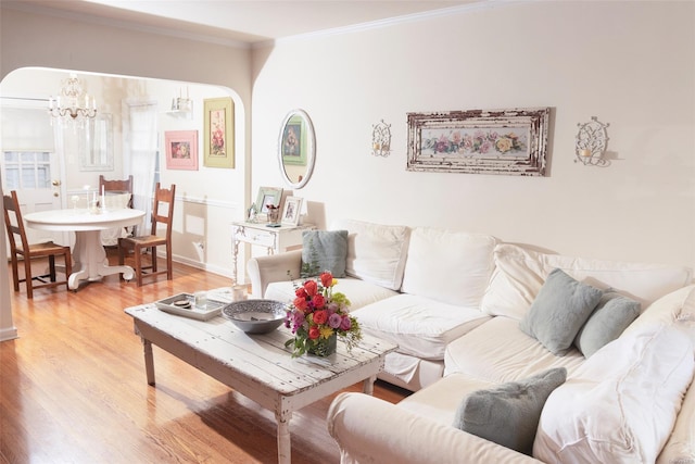 living area with arched walkways, baseboards, light wood-style floors, an inviting chandelier, and crown molding