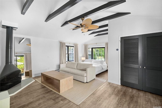 bedroom featuring hardwood / wood-style flooring, lofted ceiling with beams, ceiling fan, and a wood stove