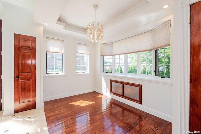 empty room with dark hardwood / wood-style floors, a raised ceiling, a notable chandelier, and crown molding