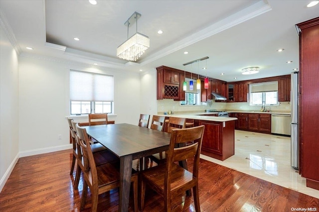 dining room with ornamental molding, light wood-type flooring, a raised ceiling, and a healthy amount of sunlight