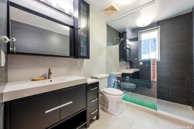 bathroom featuring tile patterned floors, toilet, tiled shower, vanity, and tile walls