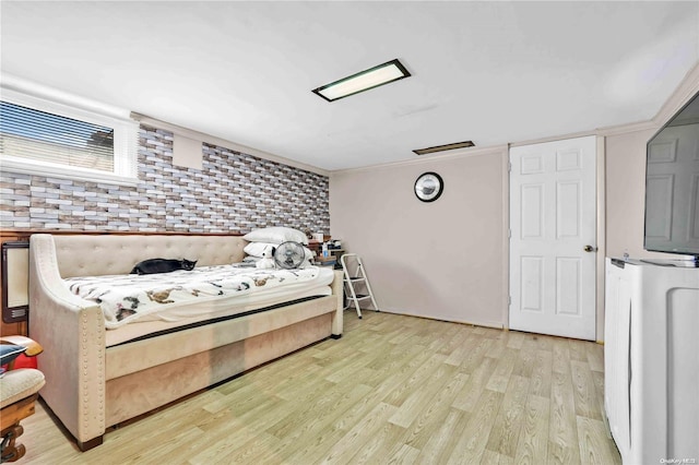 bedroom featuring light wood-type flooring and brick wall