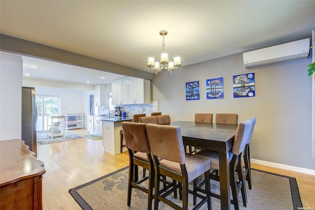 dining room with light wood-type flooring, an inviting chandelier, a wall unit AC, and sink