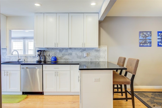 kitchen with stainless steel dishwasher, a kitchen breakfast bar, and white cabinets