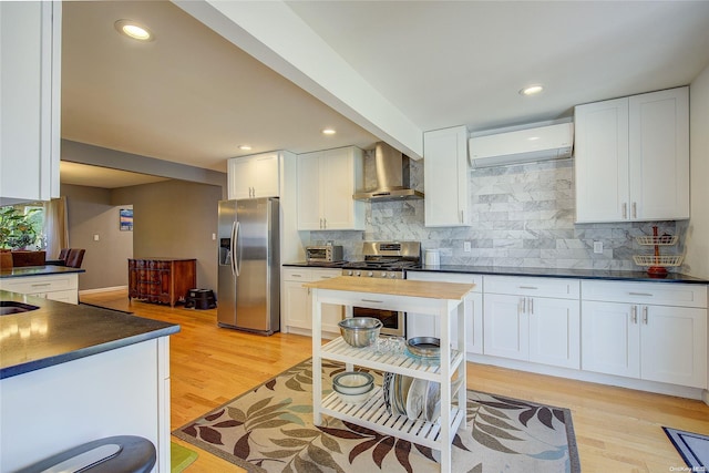 kitchen with white cabinetry, light hardwood / wood-style flooring, wall chimney range hood, and appliances with stainless steel finishes