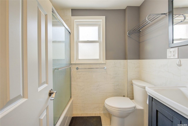 full bathroom with vanity, shower / bath combination with glass door, tile patterned floors, toilet, and tile walls