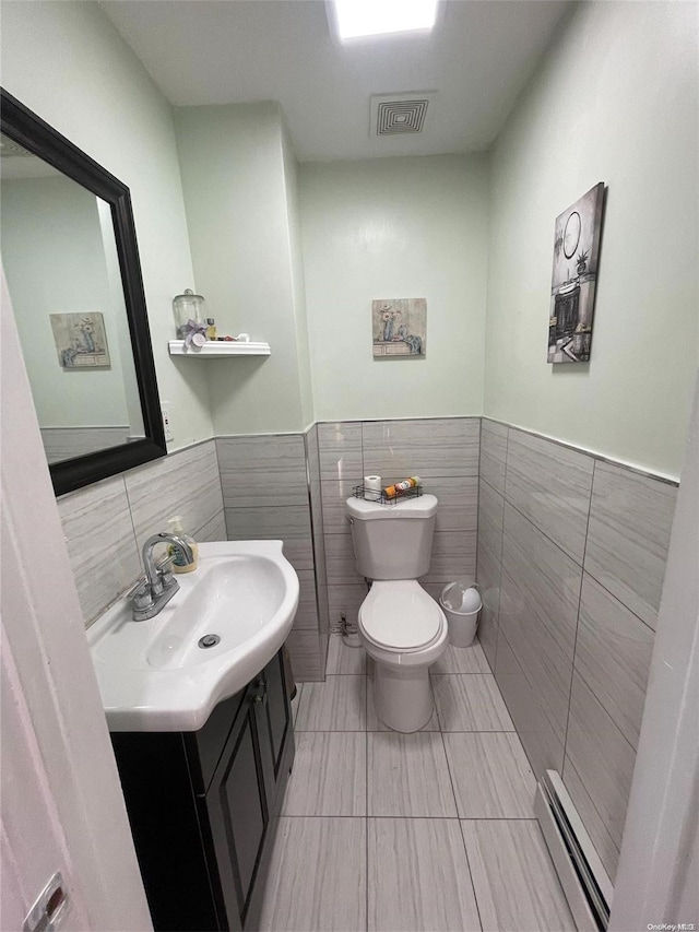 bathroom featuring vanity, tile patterned flooring, toilet, baseboard heating, and tile walls