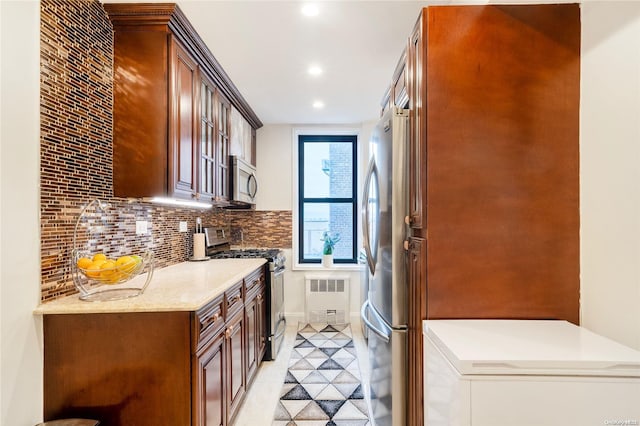 kitchen featuring light stone countertops, appliances with stainless steel finishes, tasteful backsplash, radiator, and light tile patterned floors