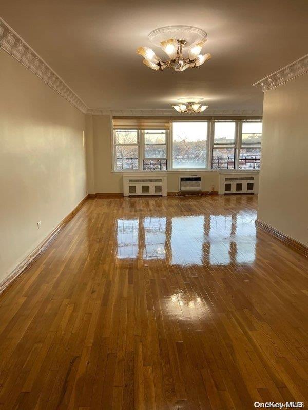 spare room featuring a chandelier, hardwood / wood-style floors, radiator heating unit, and a wall unit AC