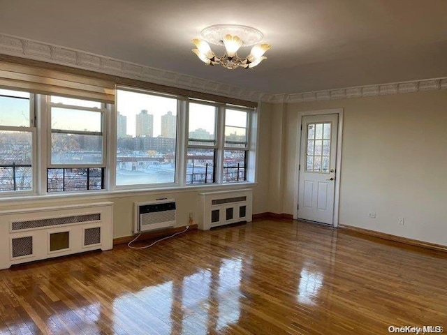 unfurnished room featuring an AC wall unit, radiator, wood-type flooring, and an inviting chandelier